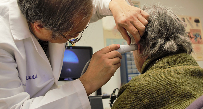 Peter Lee board certified hearing instrument specialist performs a diagnostic inspection of a patient's ear